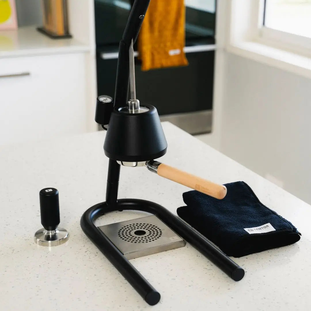 A black manual lever espresso machine with a wooden handle, a portafilter, and a black cloth on a kitchen countertop.