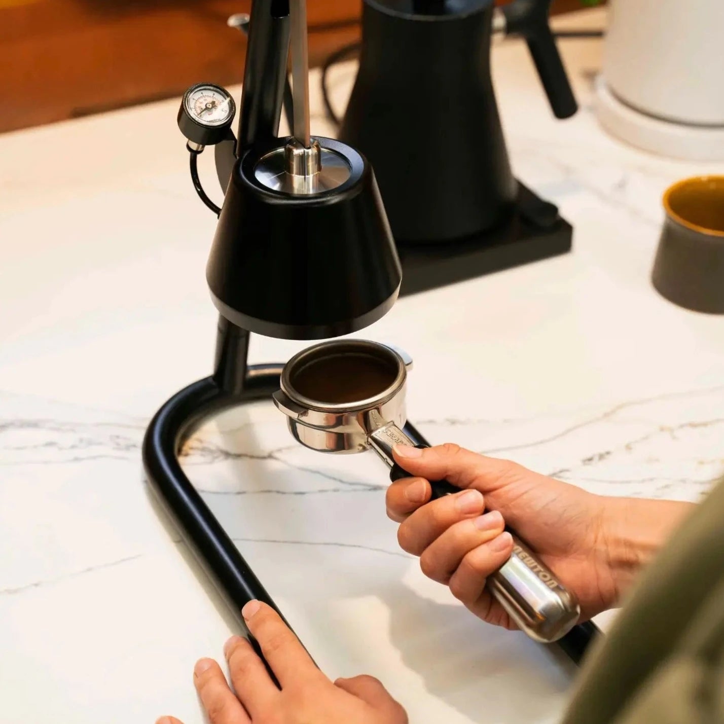 Home barista using the Newton manual espresso maker sitting on marble bench top.